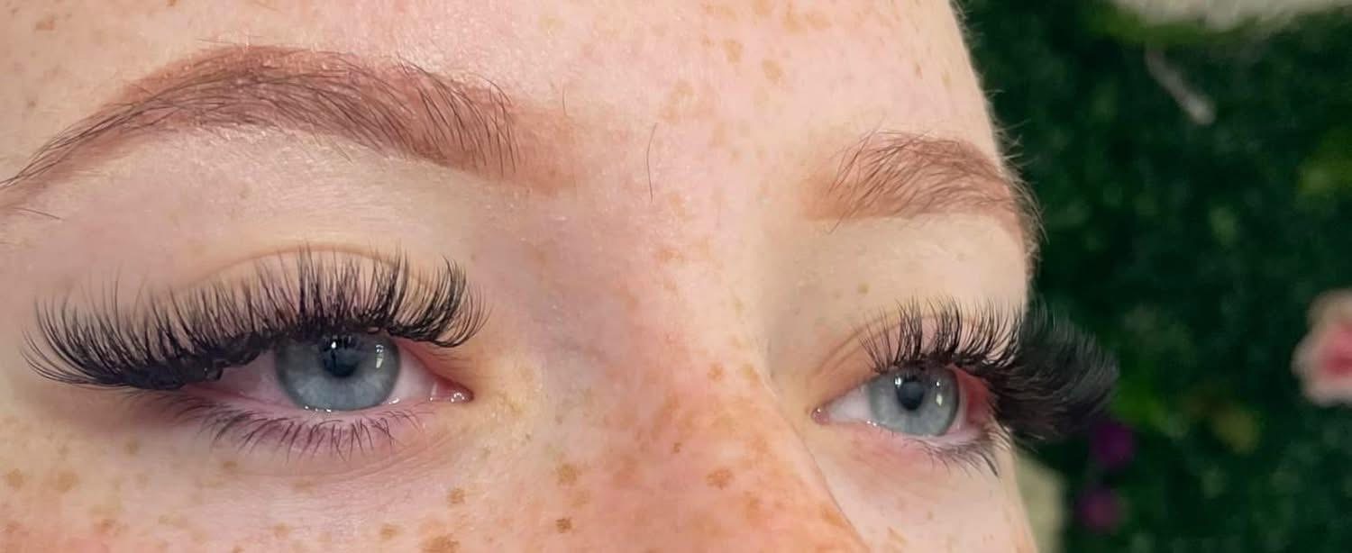 Lash extensions close-up on freckled blue eyes